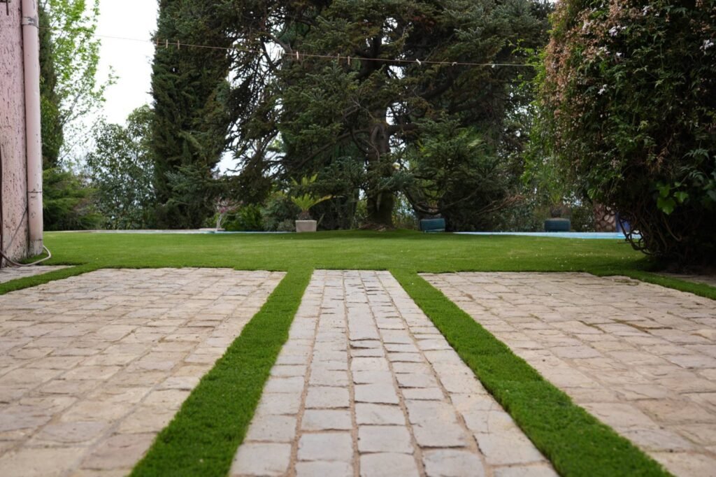 Jardín con pasto sintético Amberley 38 mm entre pasos de piedra y árboles antiguos (proyecto AF)
