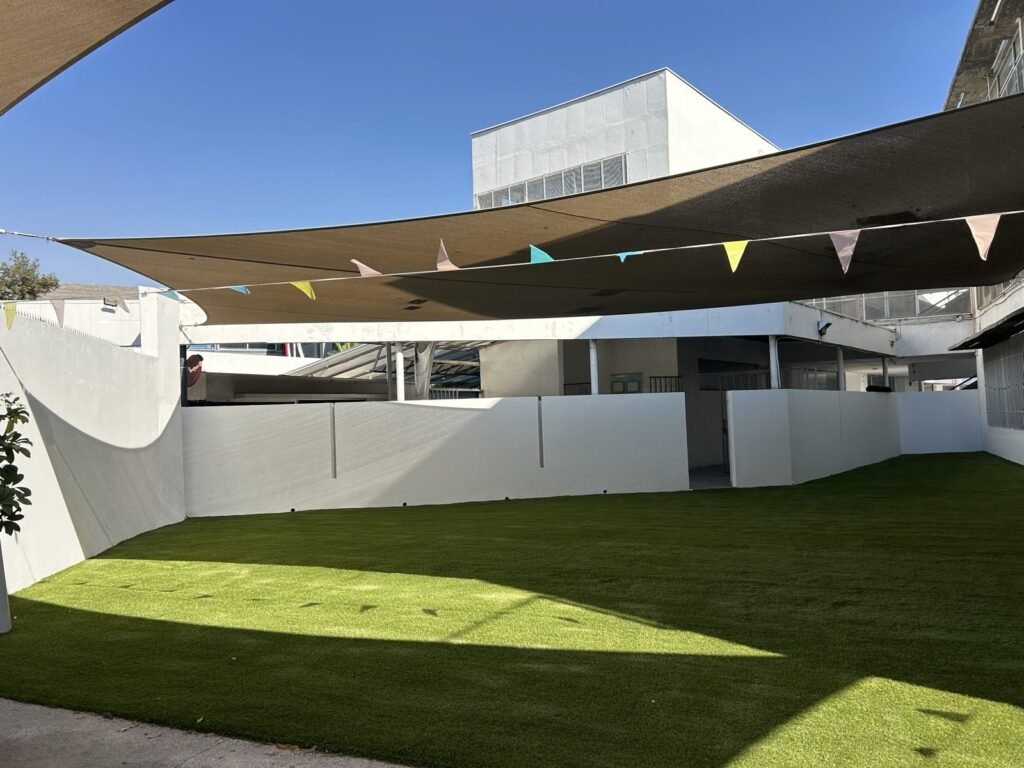 Patio de colegio con pasto sintético y malla de sombra, vista general