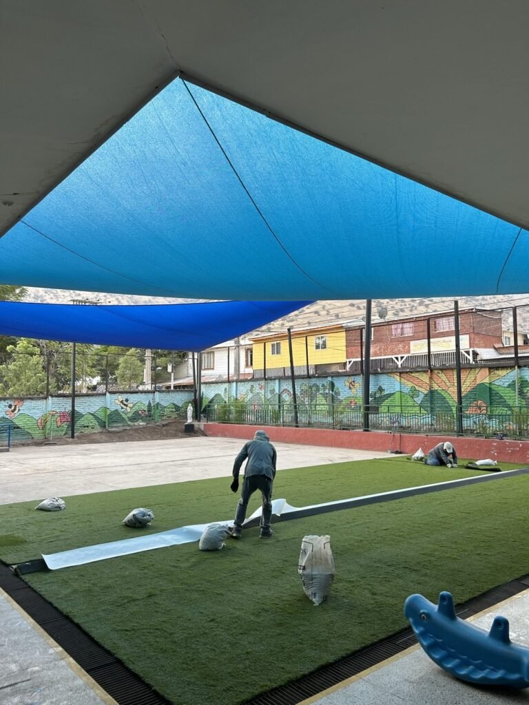 Patio de colegio con pasto sintético y malla de sombra, vista general