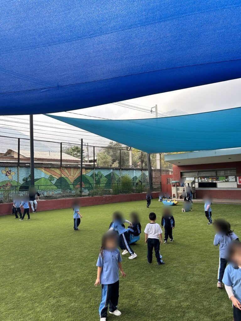 Patio de colegio con pasto sintético y malla de sombra, alumnos jugando